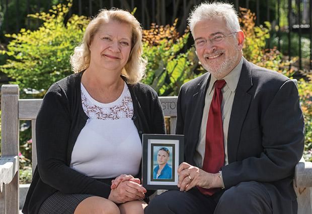 Man and woman pose while holding a photo of a young man